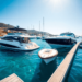 A new and a used boat side by side at a scenic marina, highlighting modern and classic designs against a backdrop of clear blue water and sunny skies.