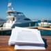 A serene marina with a docked boat, clear blue skies, and gentle waves. In the foreground, important documents are neatly arranged on a wooden tabl...