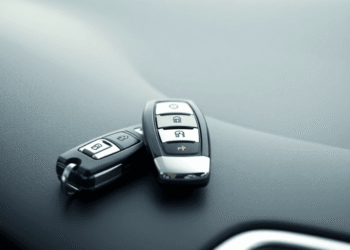 Close-up of a shiny car key fob on a smooth dashboard with a blurred sleek vehicle reflection in soft natural light.