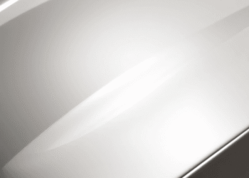 Shiny car hood reflecting sunlight with a subtle glowing protective film being applied, set against a bright, clean background.